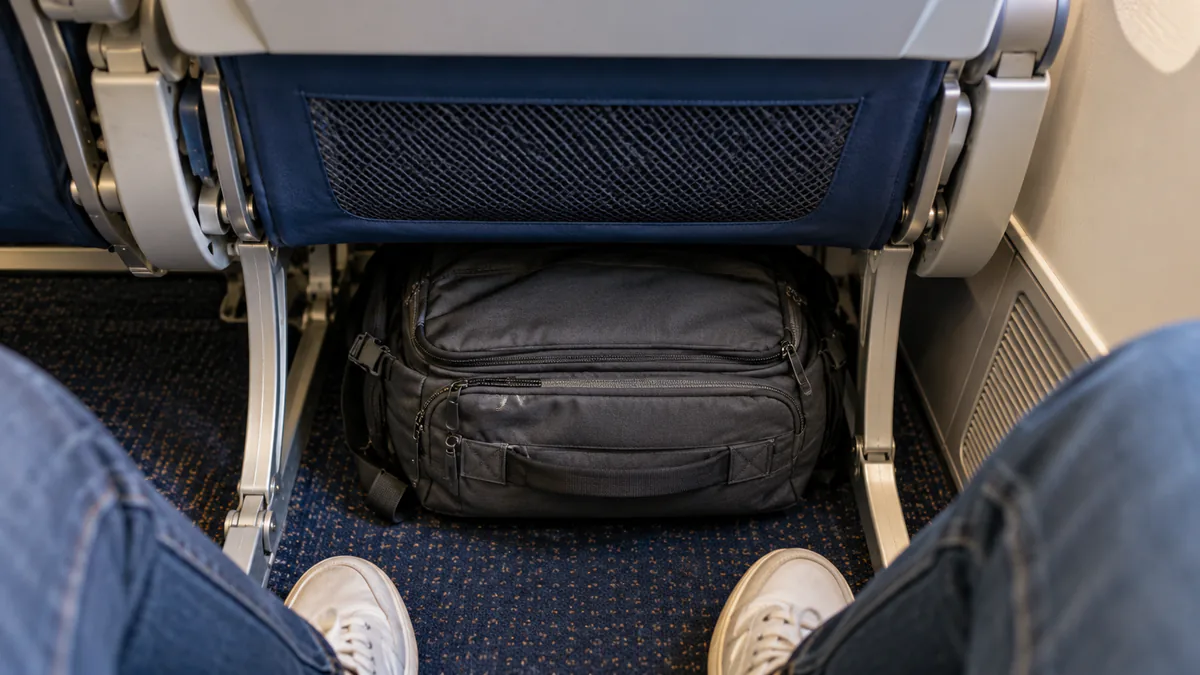 Mochila pequeña colocada debajo del asiento delantero de un avión